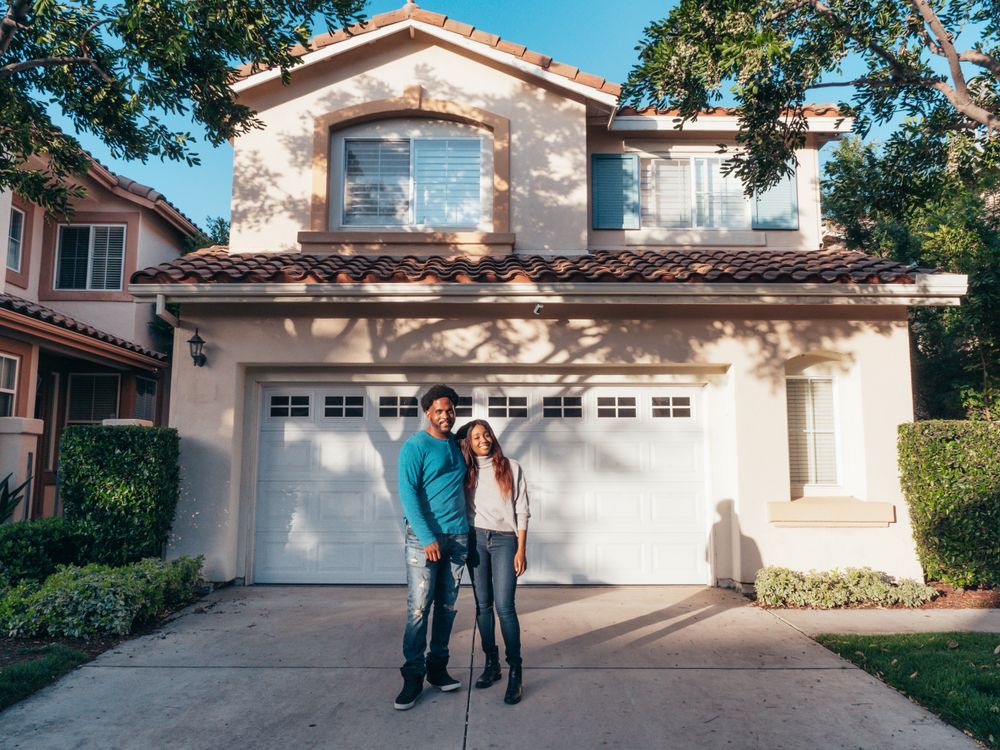 Happy homeowners standing in front of their house after getting an instant roofing quote